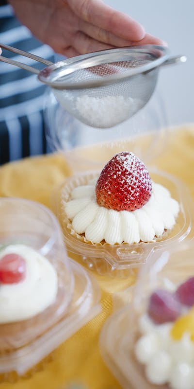 A delicious strawberry cupcake being topped with powdered sugar by a hand using a sieve.