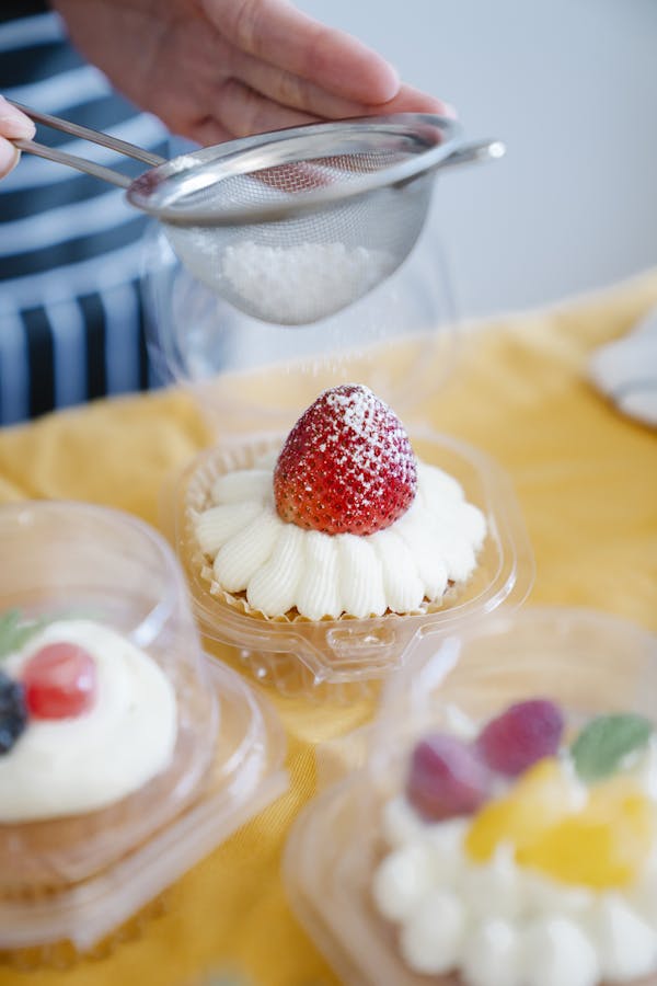 A delicious strawberry cupcake being topped with powdered sugar by a hand using a sieve.