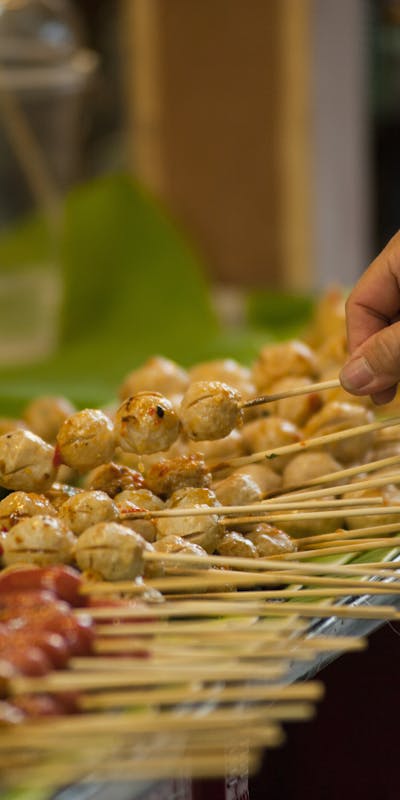 A hand selects skewers at a vibrant Thai street food market, highlighting local culinary culture.