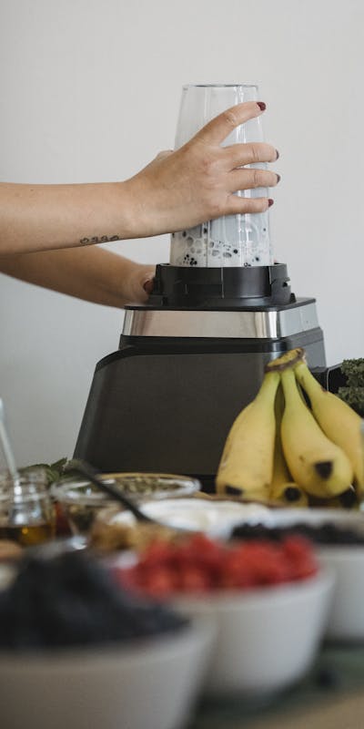 A woman using a blender to prepare a nutritious fruit smoothie with fresh ingredients.