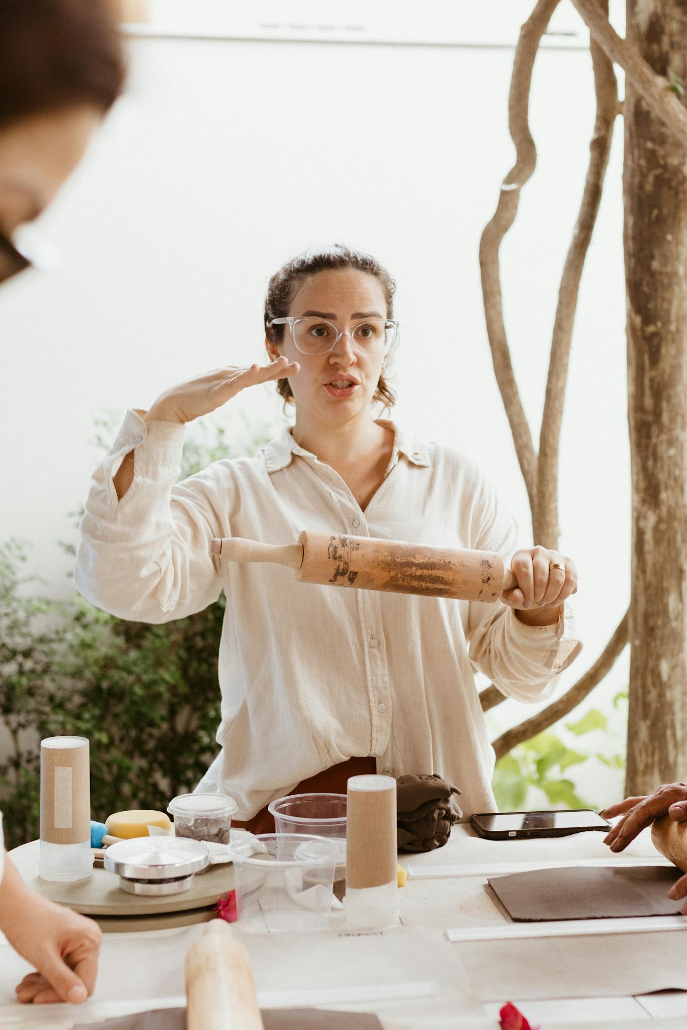 Adult woman in glasses instructing a baking class using a rolling pin indoors.