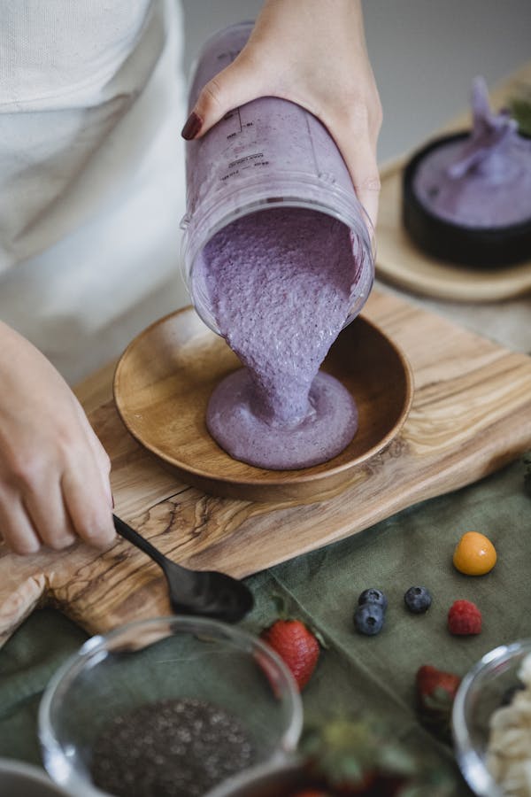 Close-up of a berry smoothie being poured into a wooden bowl, surrounded by fresh ingredients.