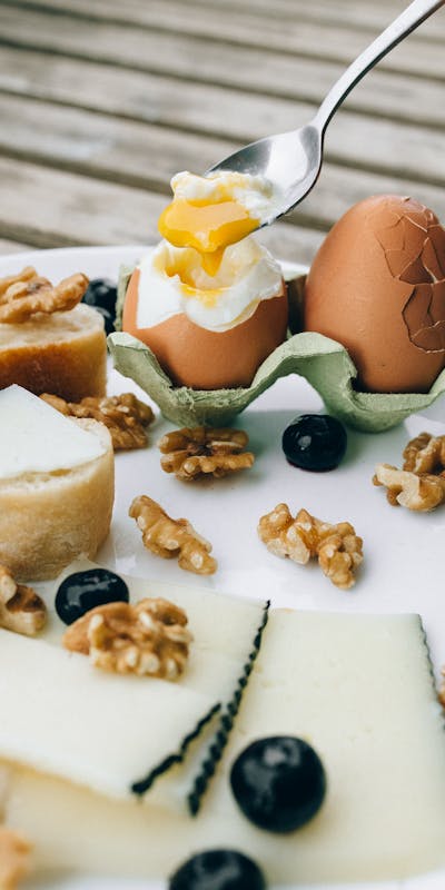 Delicious gourmet breakfast with soft-boiled eggs, cheese, nuts, and fruits on a rustic plate.
