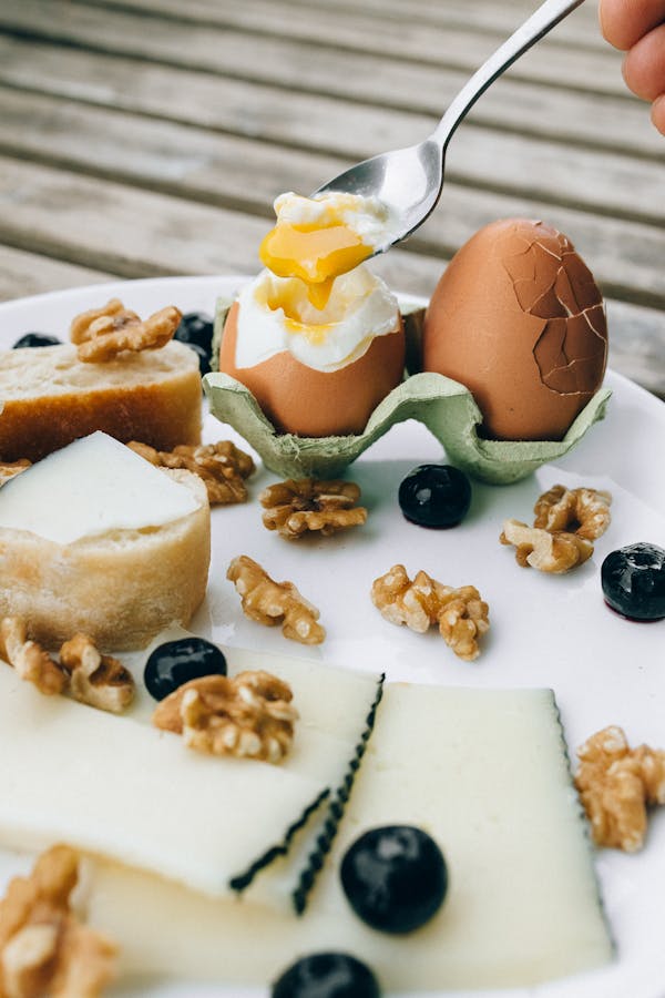 Delicious gourmet breakfast with soft-boiled eggs, cheese, nuts, and fruits on a rustic plate.