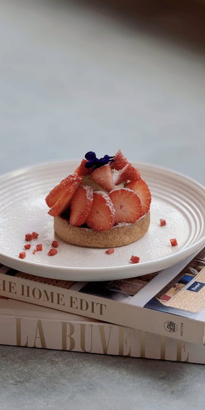 Elegant strawberry tart on a white plate atop stacked books, showcasing chic food styling.