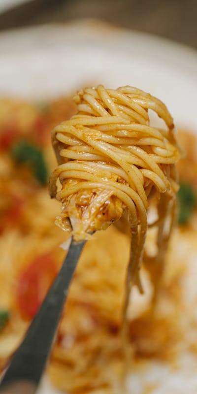 From above fork with tasty fresh spaghetti in tomato sauce served on white plate