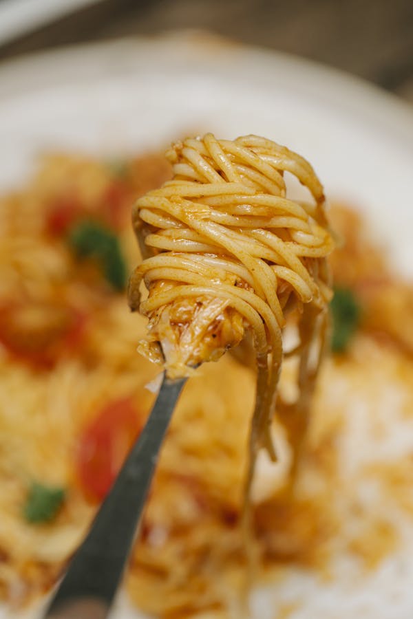 From above fork with tasty fresh spaghetti in tomato sauce served on white plate