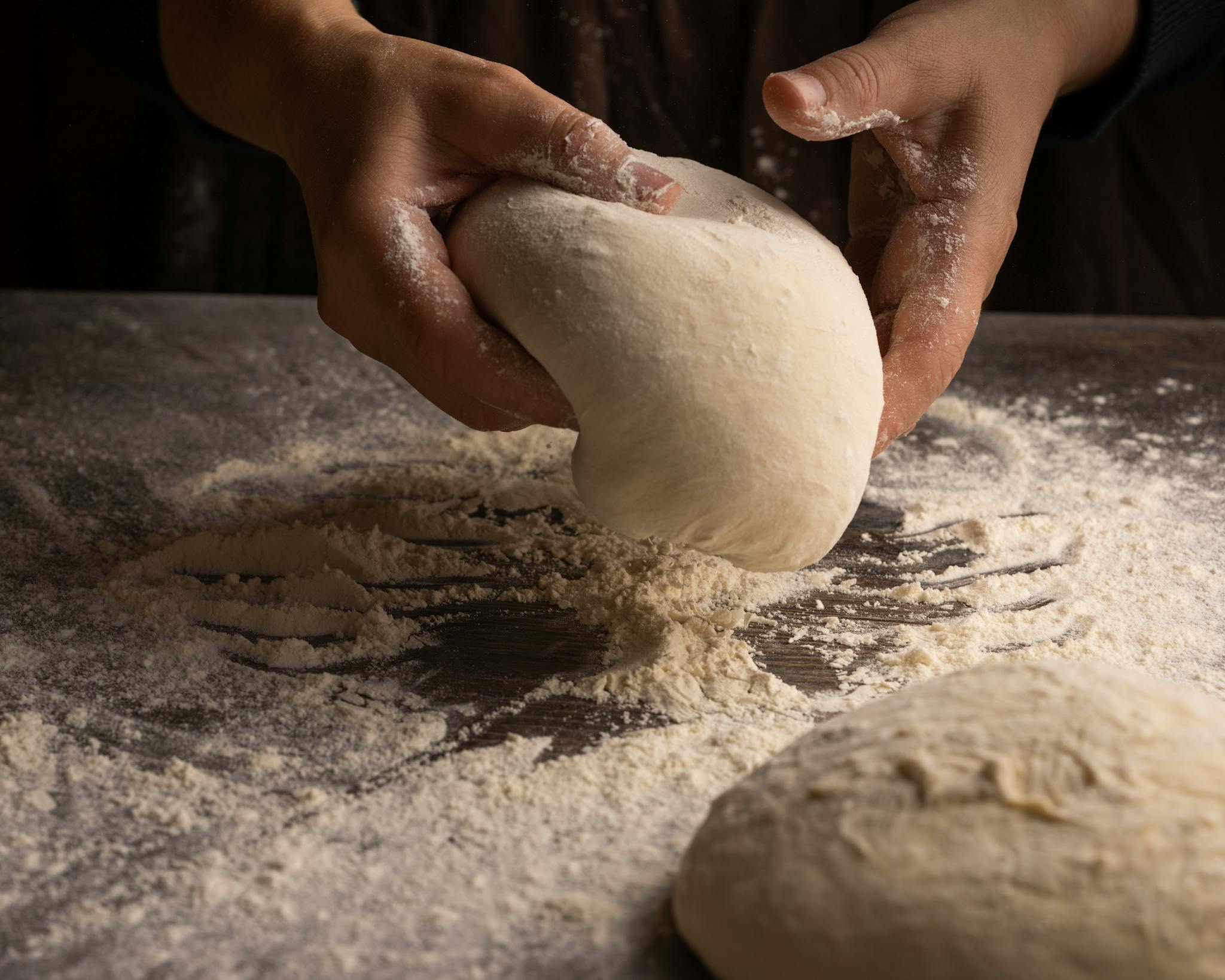Hands kneading dough on a floured surface, capturing artisan bread making.