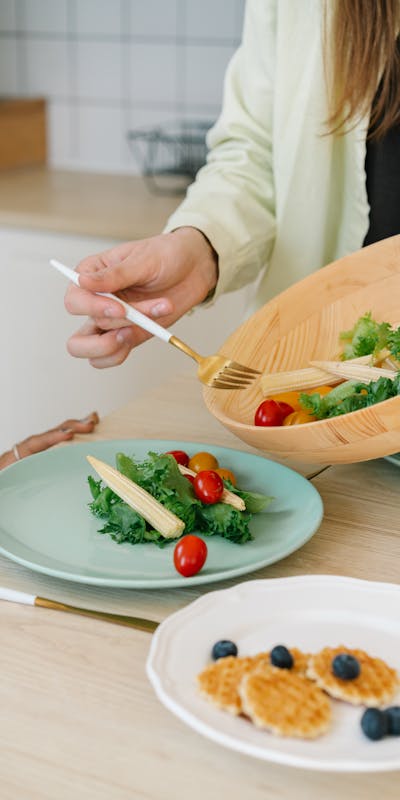 Person serving a fresh salad with baby corn, tomatoes, and greens for a healthy meal.