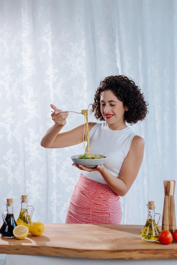 Young woman with curly black hair enjoying a bowl of Italian pasta indoors.